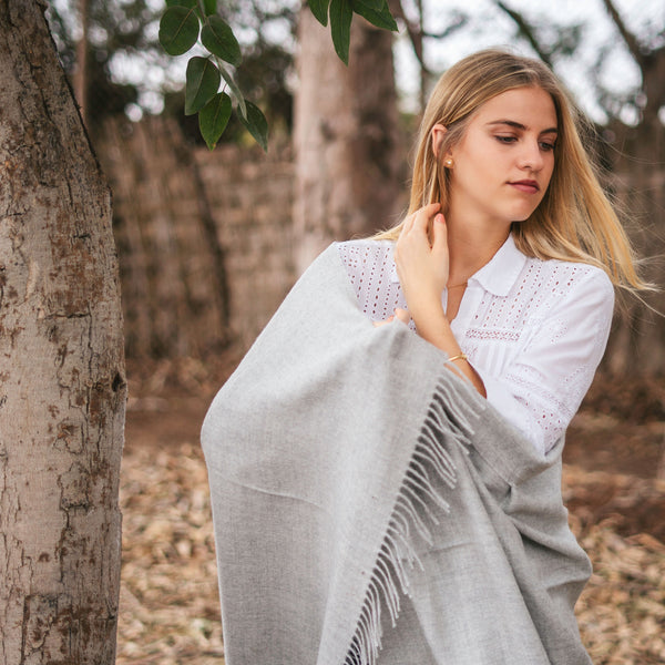 Model standing wrapped in the Storm grey throw beside eucalyptus wood