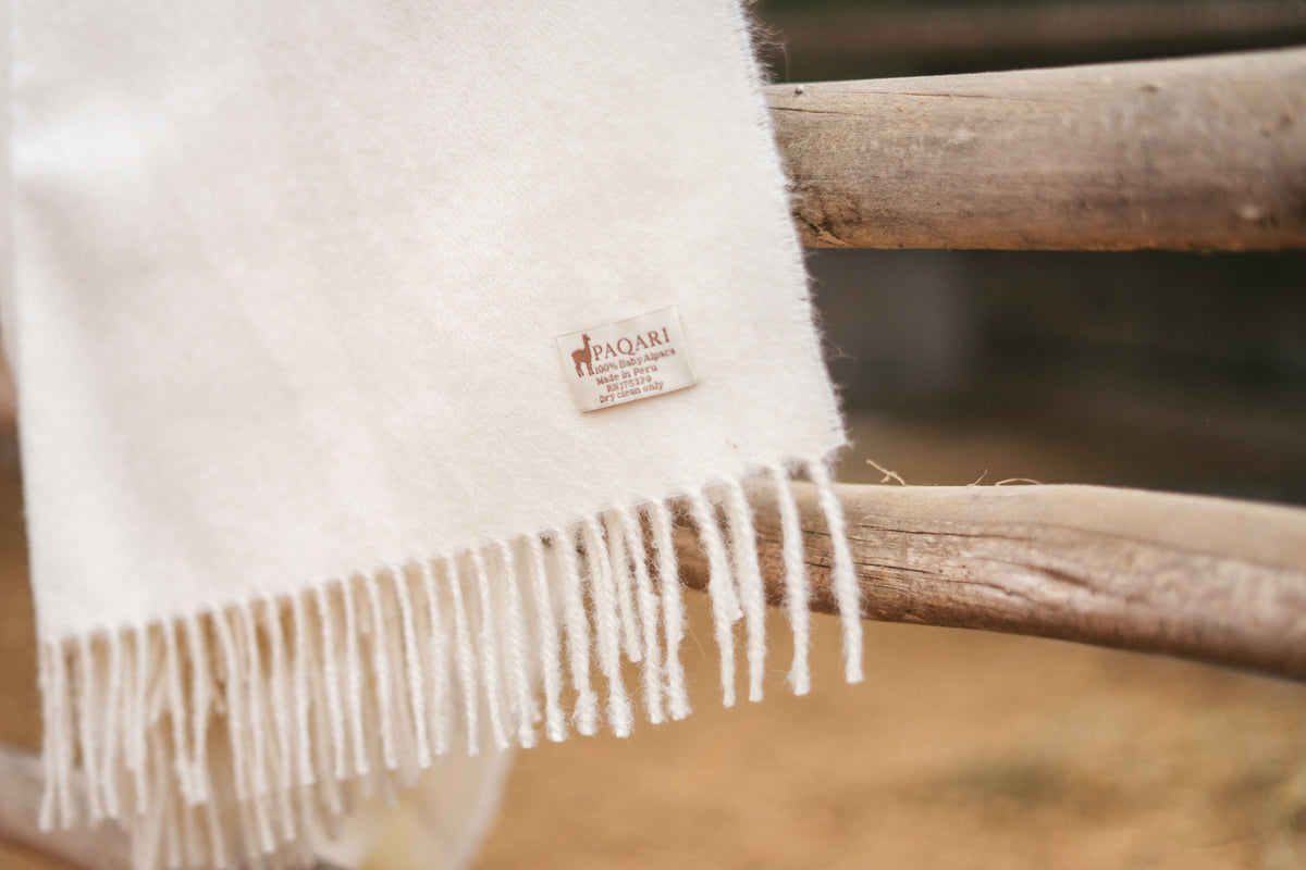 Ivory Paqari baby alpaca throw with hand-knotted fringe draped over a wooden fence