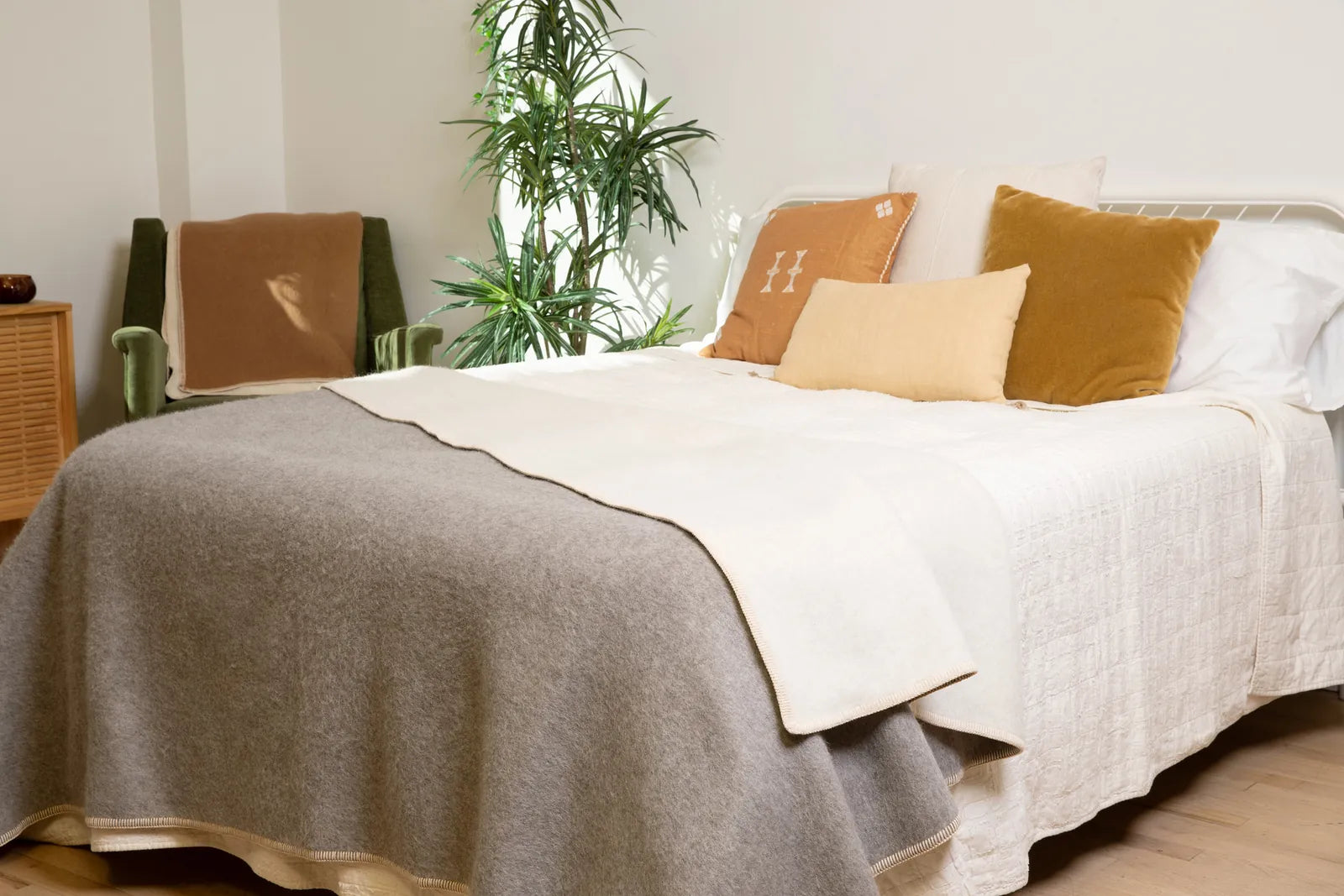 Heather gray side of the Paqari blanket spread across a bed, with the cream stitched edge visible