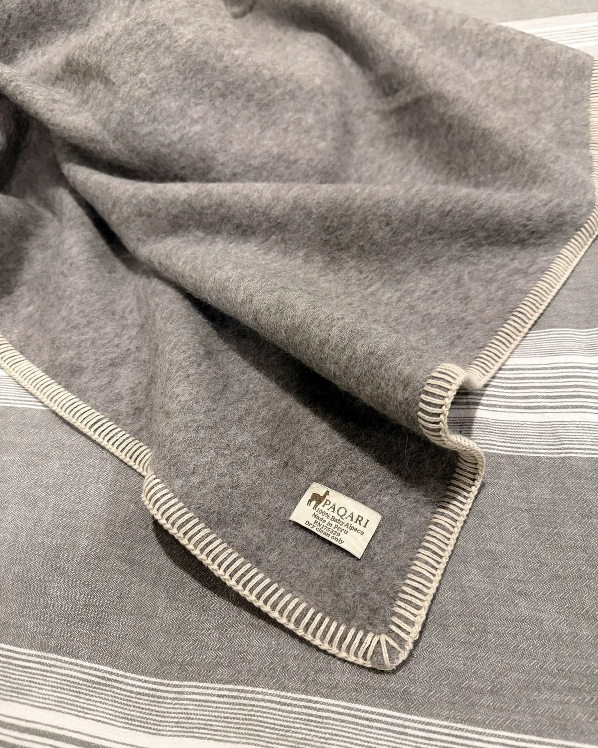 Finished Paqari heather gray baby alpaca blanket with cream blanket-stitch edge and one sewn corner tag